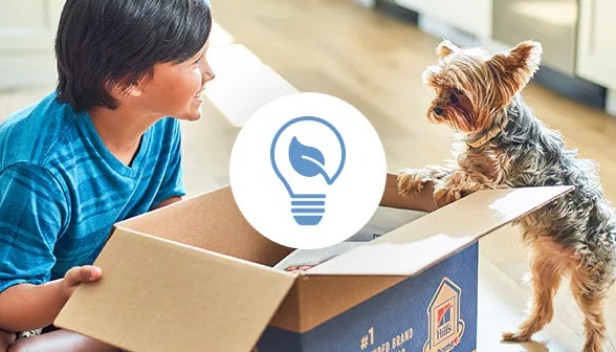 A young boy and a dog looking at recyclable Hill’s box
with a reducing waste icon on it